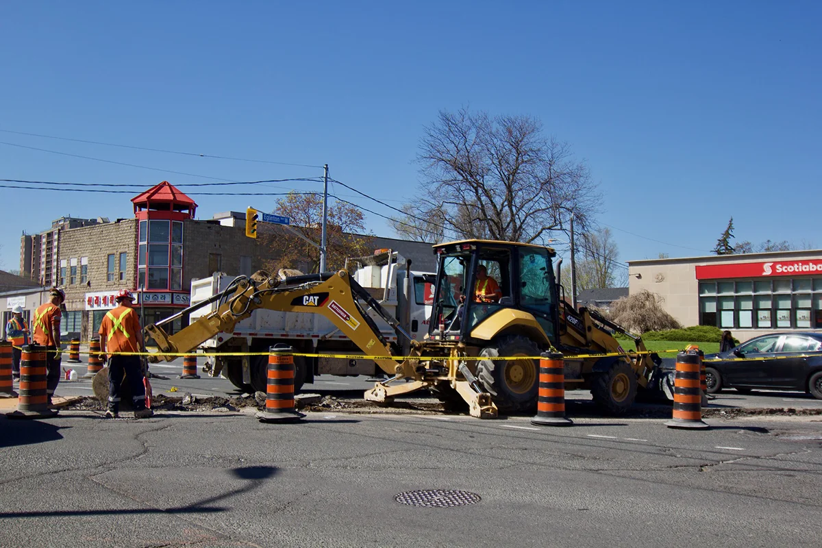 Backhoe digging up road with lanes closed with construction bollards and tape