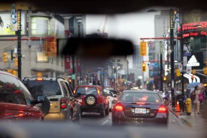 View through windshield of car with rearview mirror in foreground and stopped cars in heavy traffic.