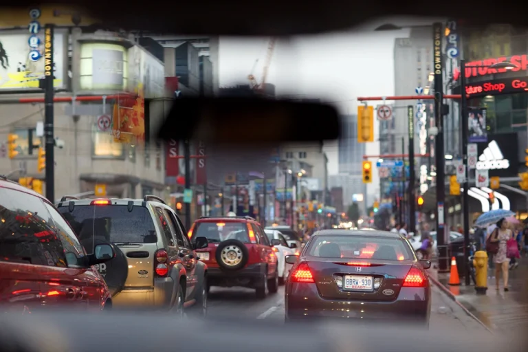 View through windshield of car with rearview mirror in foreground and stopped cars in heavy traffic.